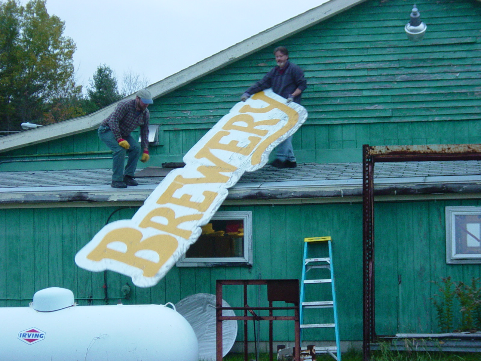 Two people on the roof lowering the BREWERY sign